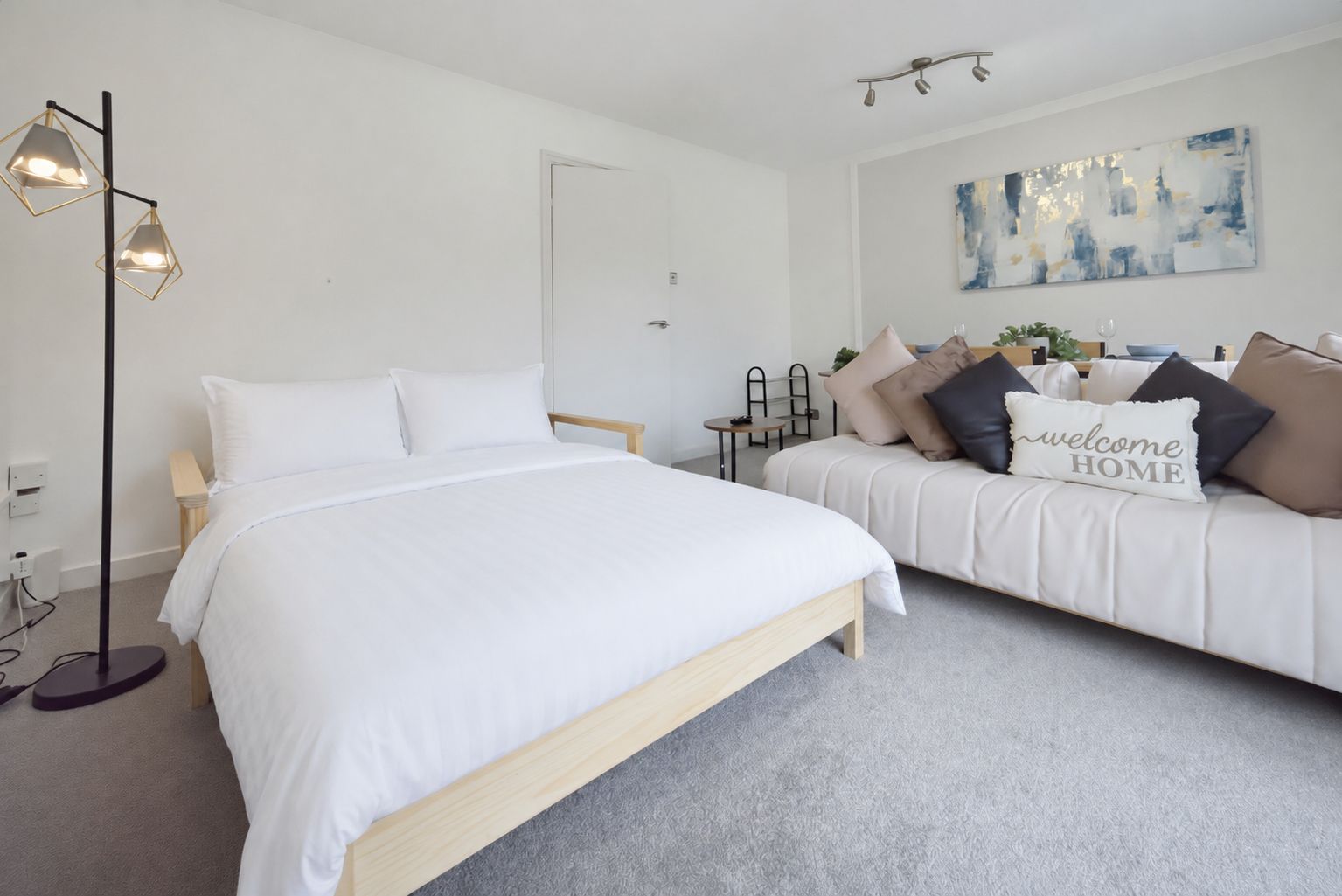 Bright white bedroom with a bed, sofa, floor lamp, and wall art on light carpet