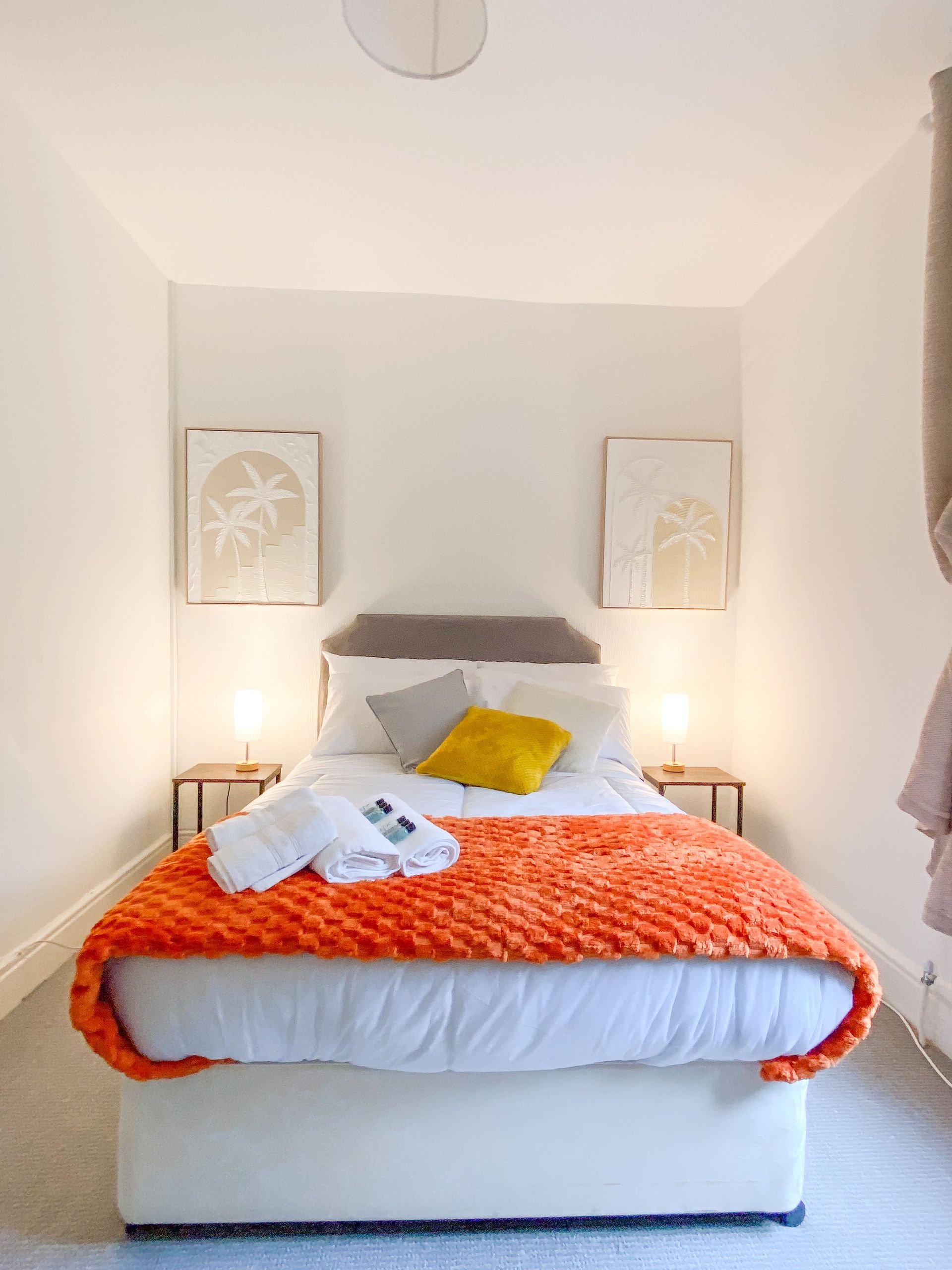 Cozy white bedroom with orange bedspread, yellow accent pillow, and soft bedside lamps