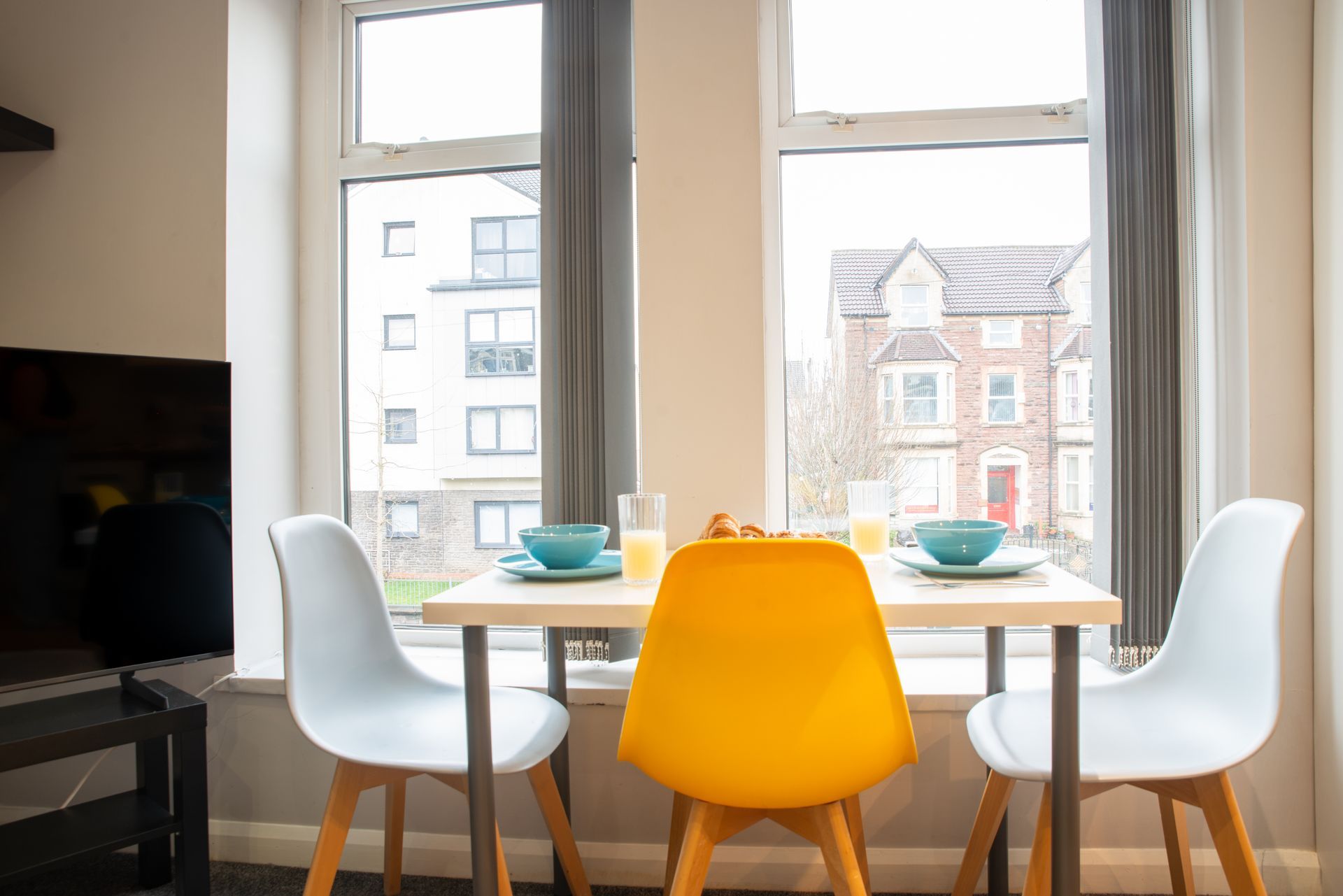Dining table by a bright window with four colorful chairs and place settings
