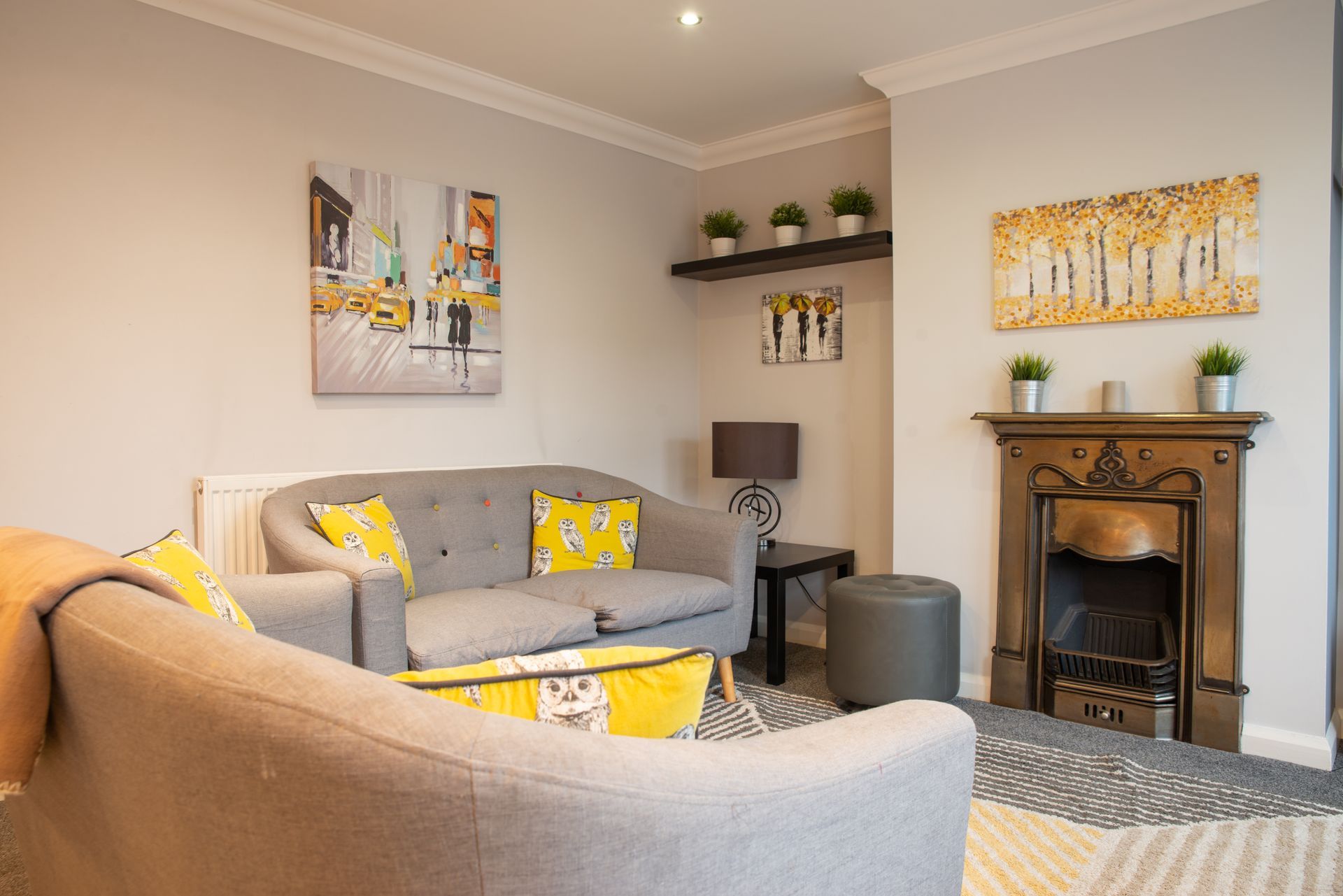 Cozy living room with gray sofa, yellow accents, fireplace, and wall art