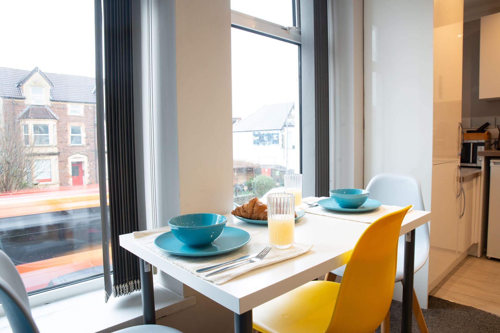 Bright dining nook with yellow chair, blue bowls, and a small table by large windows.