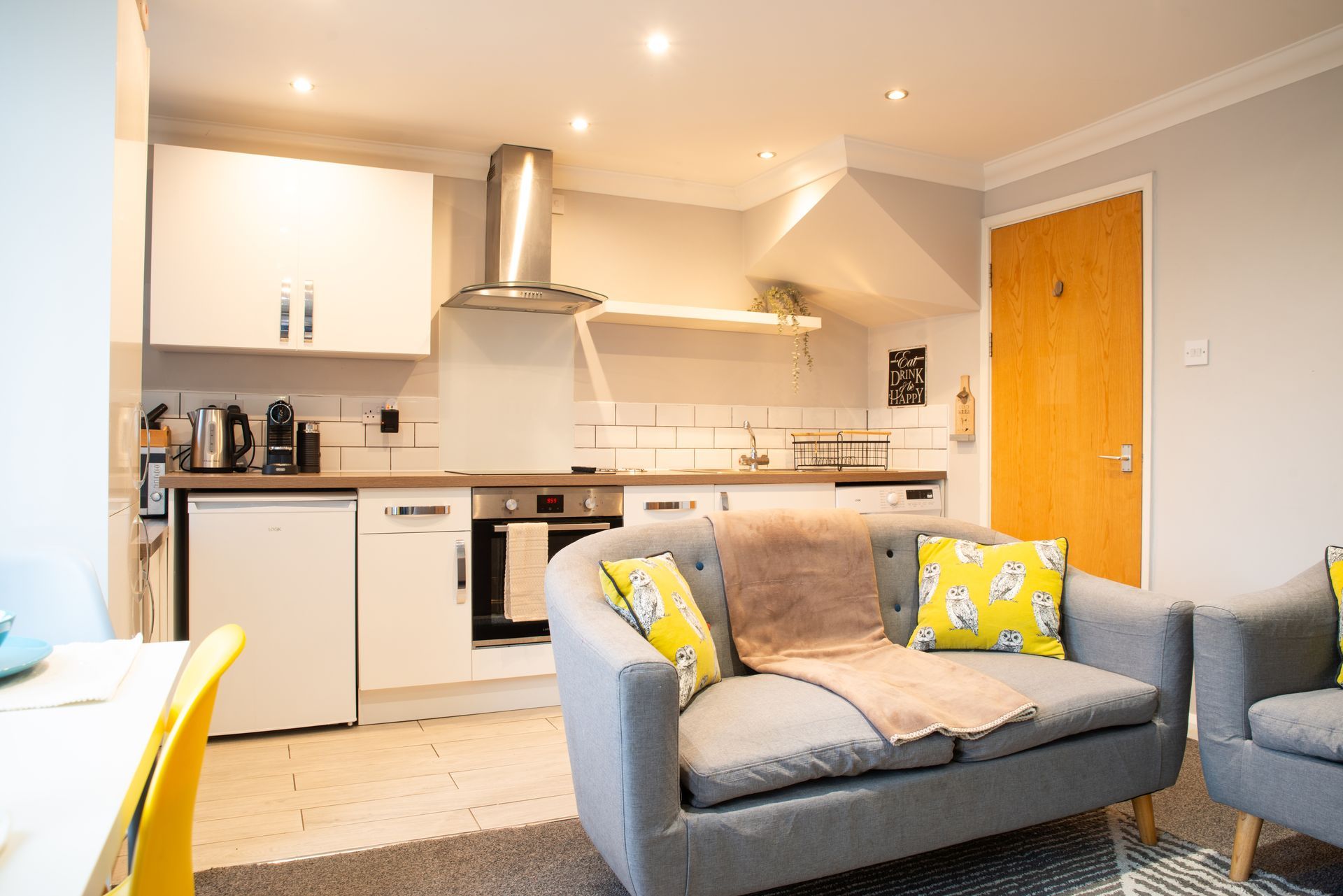 Bright modern kitchen and living room with gray sofa, yellow cushions, and wooden door