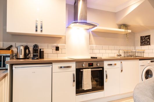 Modern white kitchen with wooden countertops, stainless hood, dishwasher, oven, and washing machine