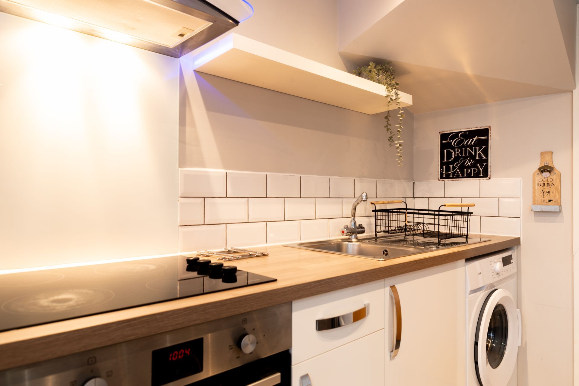 Modern compact kitchen with wooden countertops, white cabinets, tiled backsplash, stove, sink, and laundry machine
