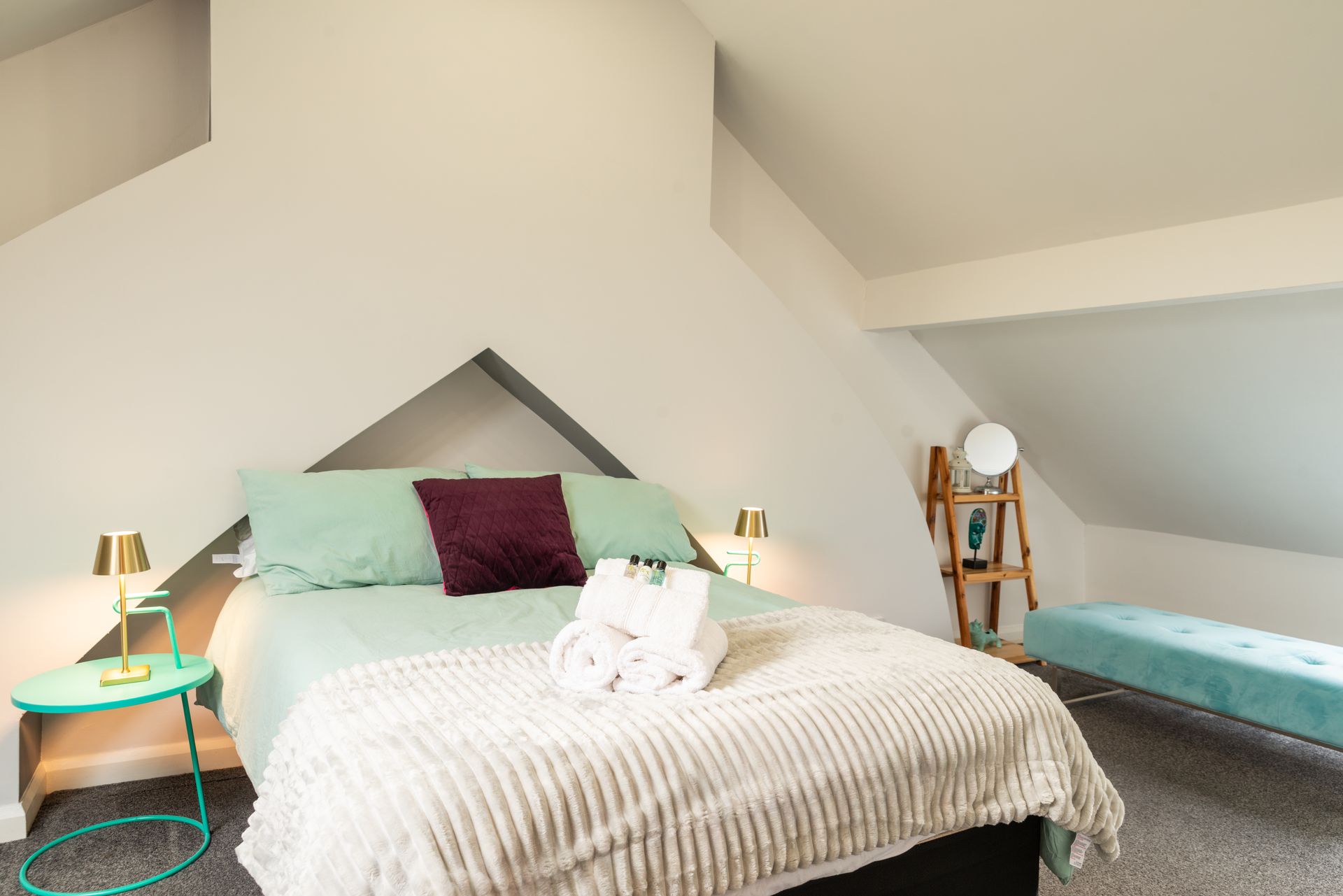 Bright attic bedroom with a bed, mint bedding, teal chair, and a turquoise daybed under sloped ceilings