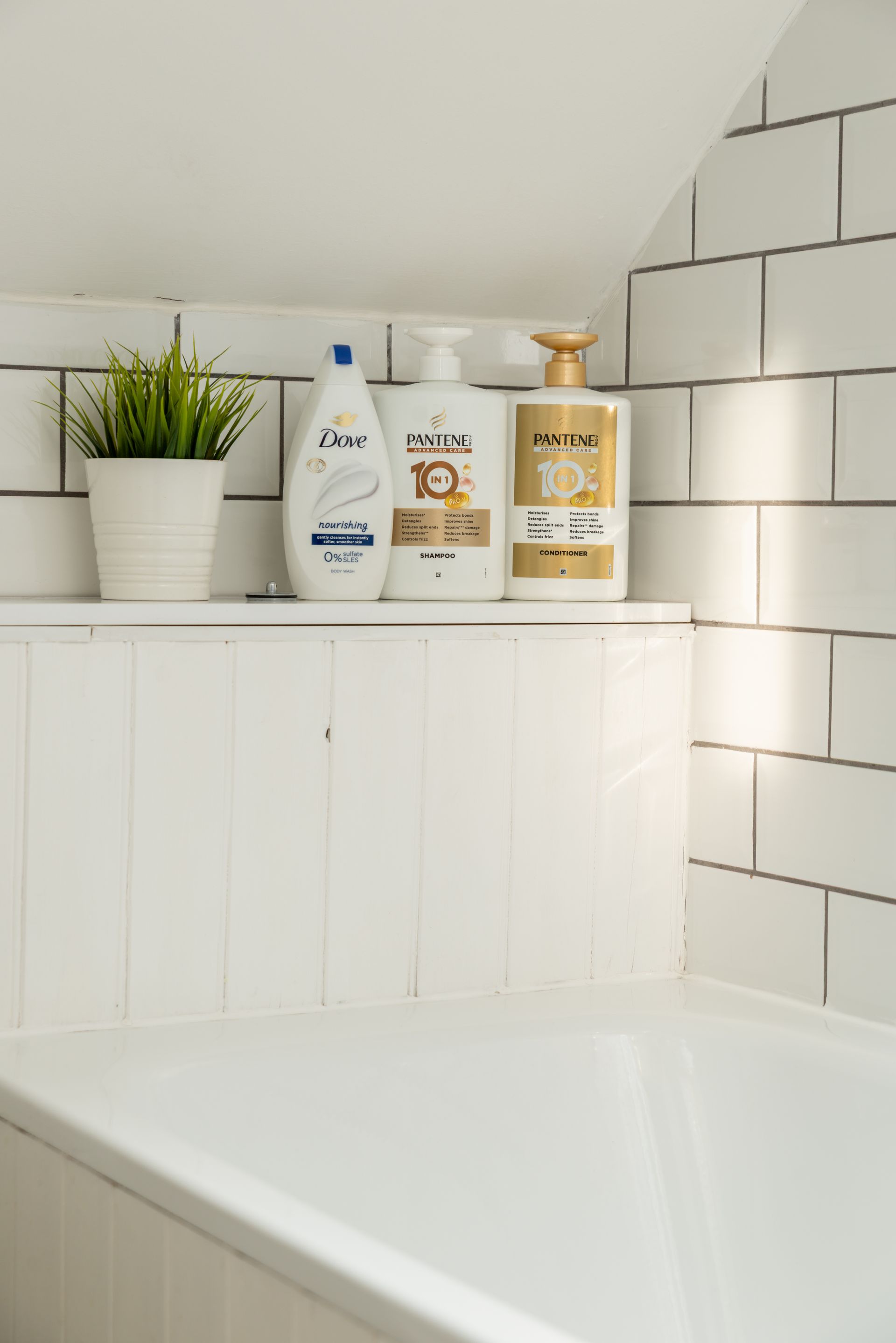 White bathtub corner with tiled wall, shelf, and bath products beside a potted plant