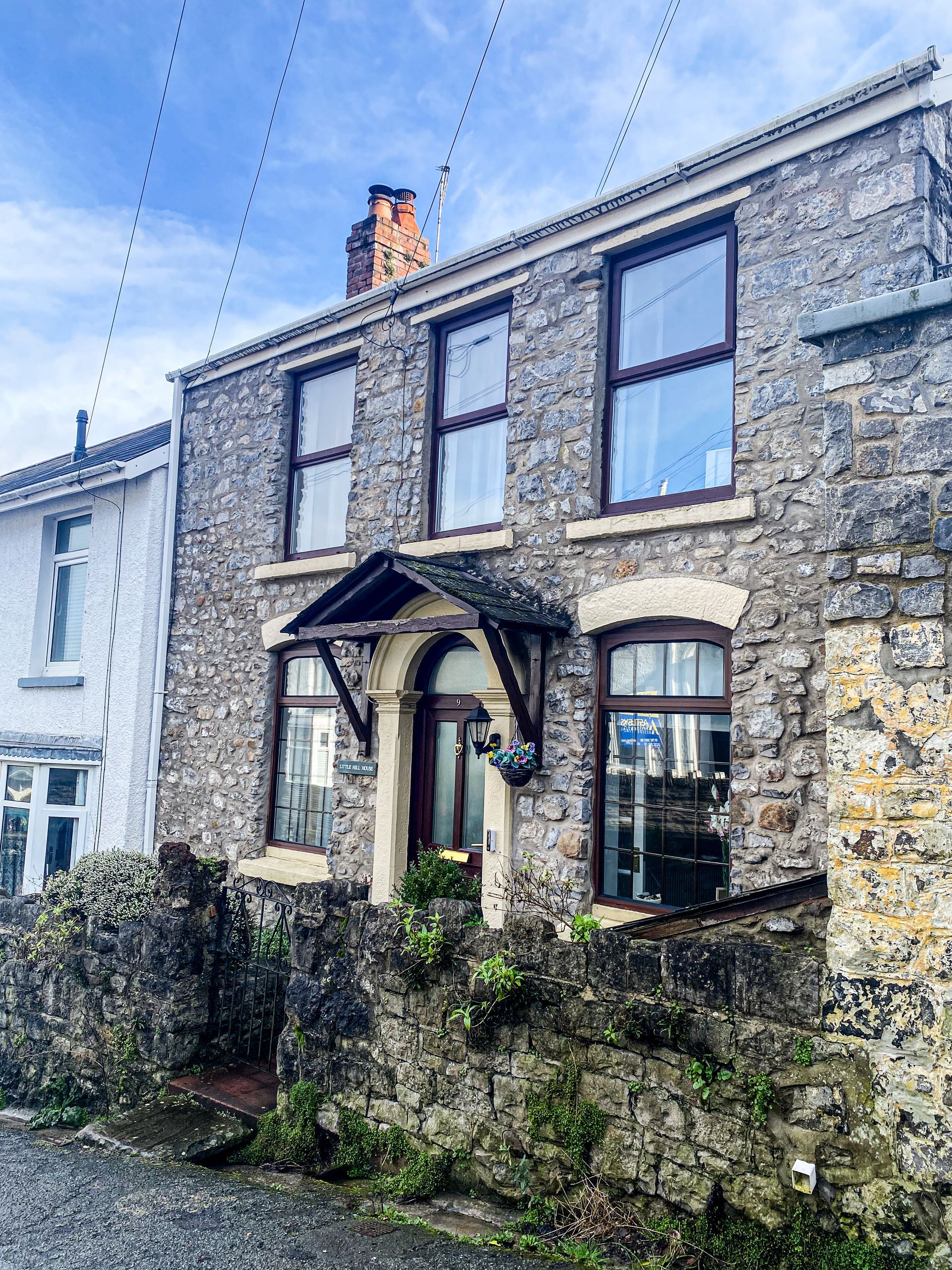Stone cottage with arched porch and bay windows on a rainy street