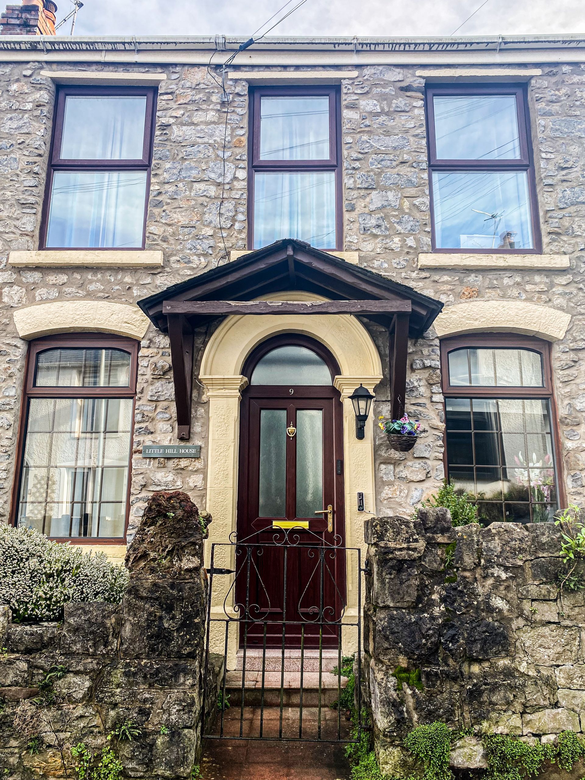 Stone townhouse with a red front door, arched entry, and two upper windows behind a low stone wall.