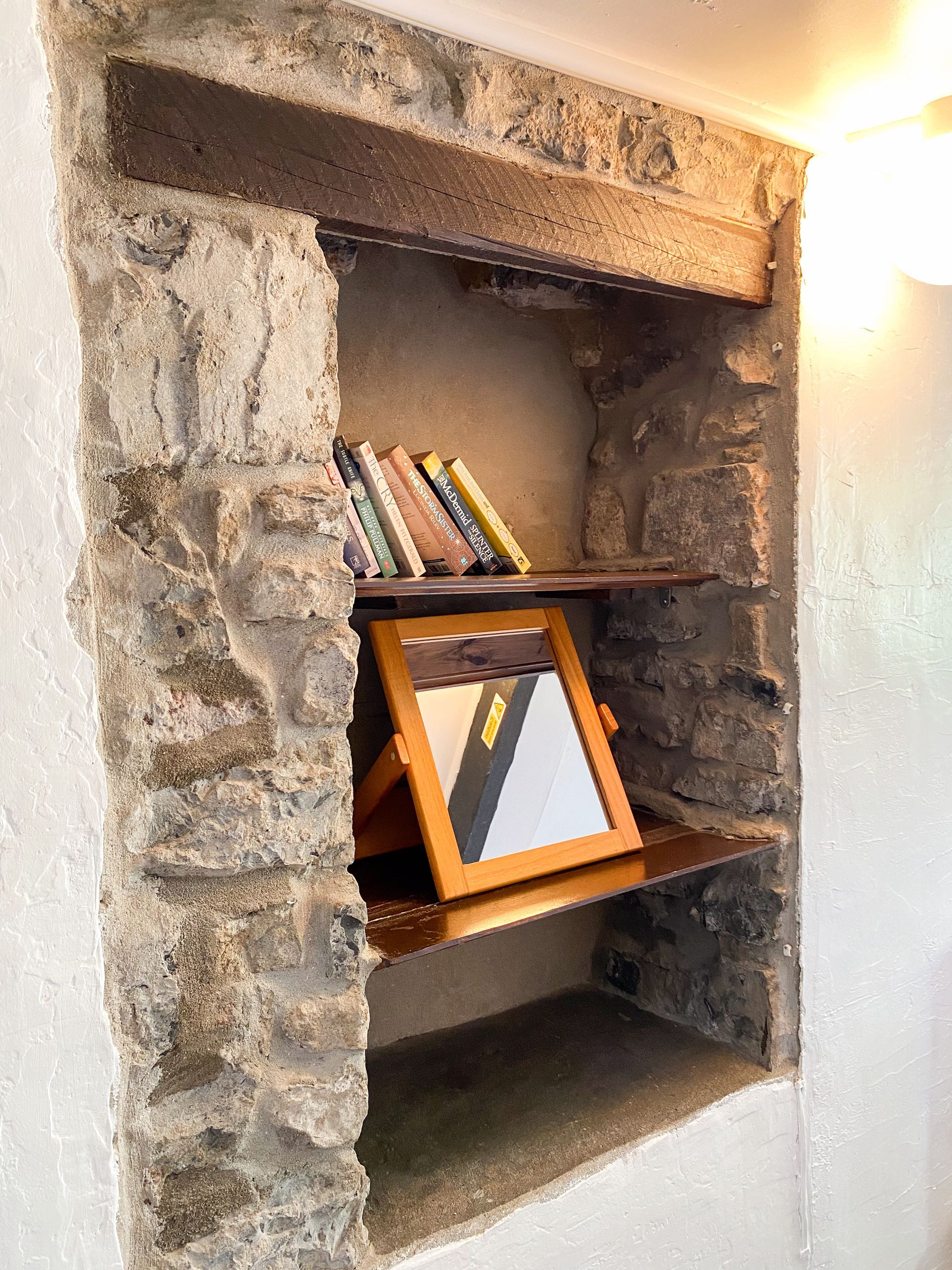 Stone wall niche shelf with books and a framed photo beside a lit wall lamp