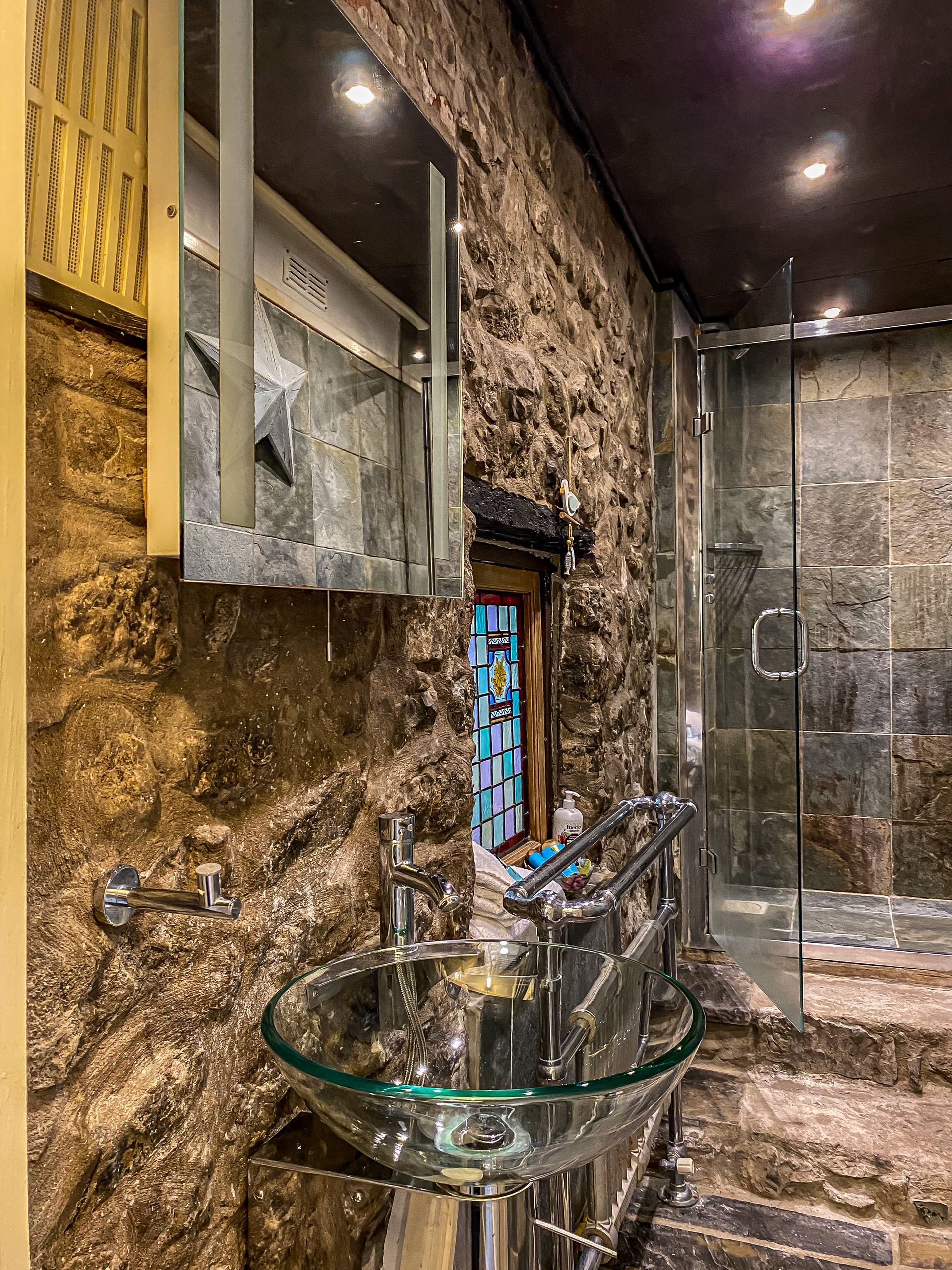 Modern bathroom vanity with glass sink, chrome faucet, and stone-textured walls