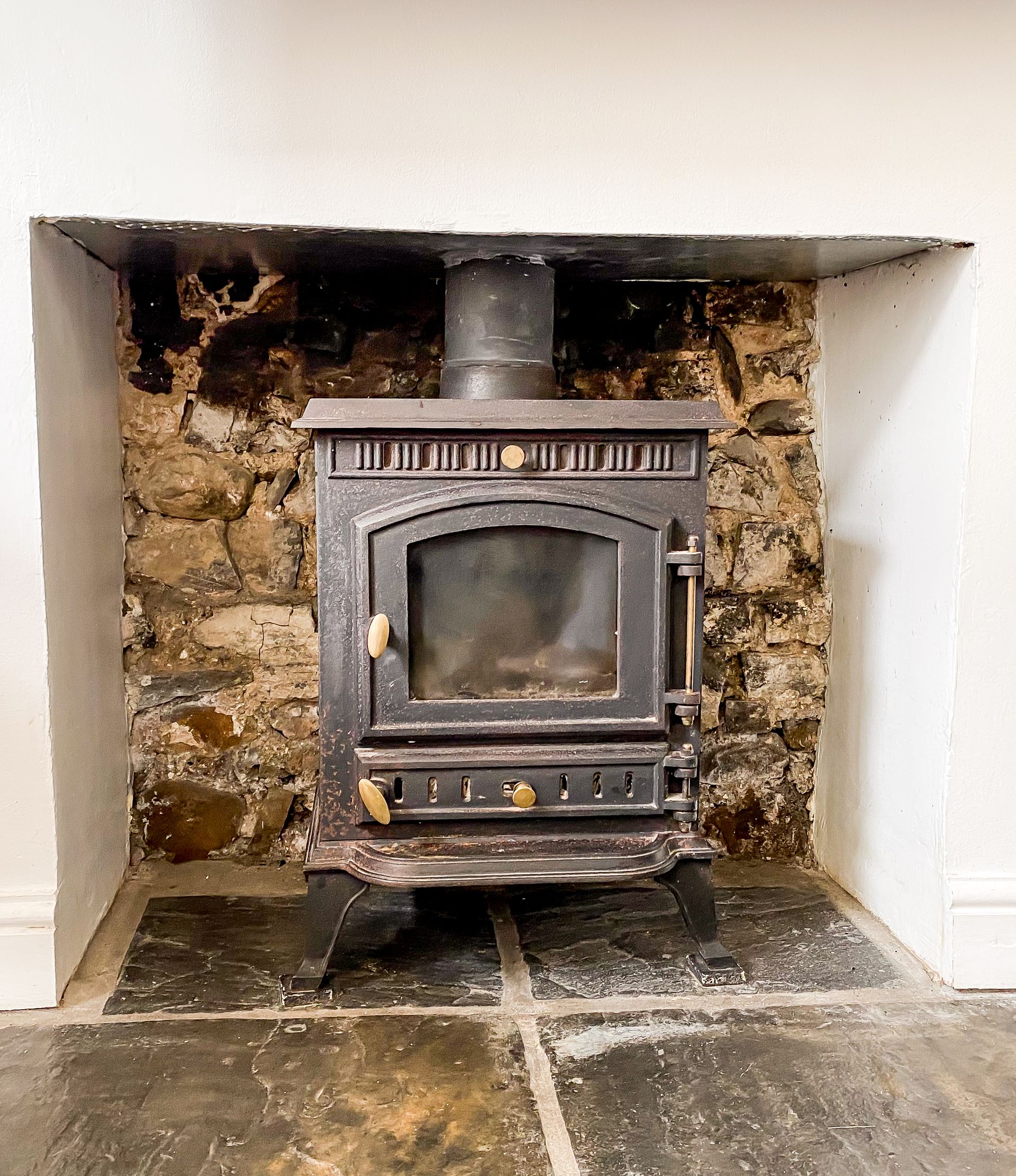 Old black wood-burning stove set in a worn stone fireplace alcove with soot-stained walls