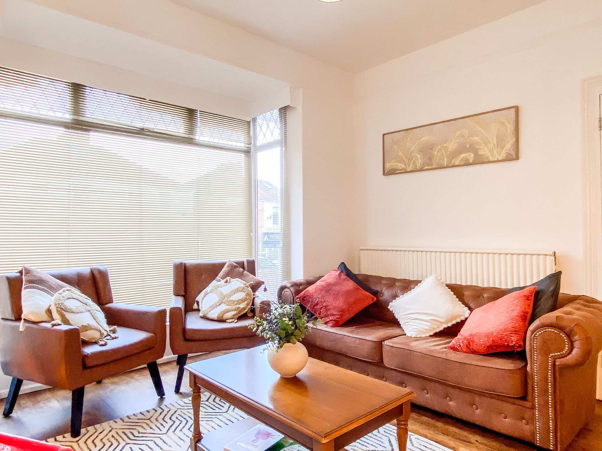 Bright living room with brown sofa, two armchairs, coffee table, and sunlight through blinds