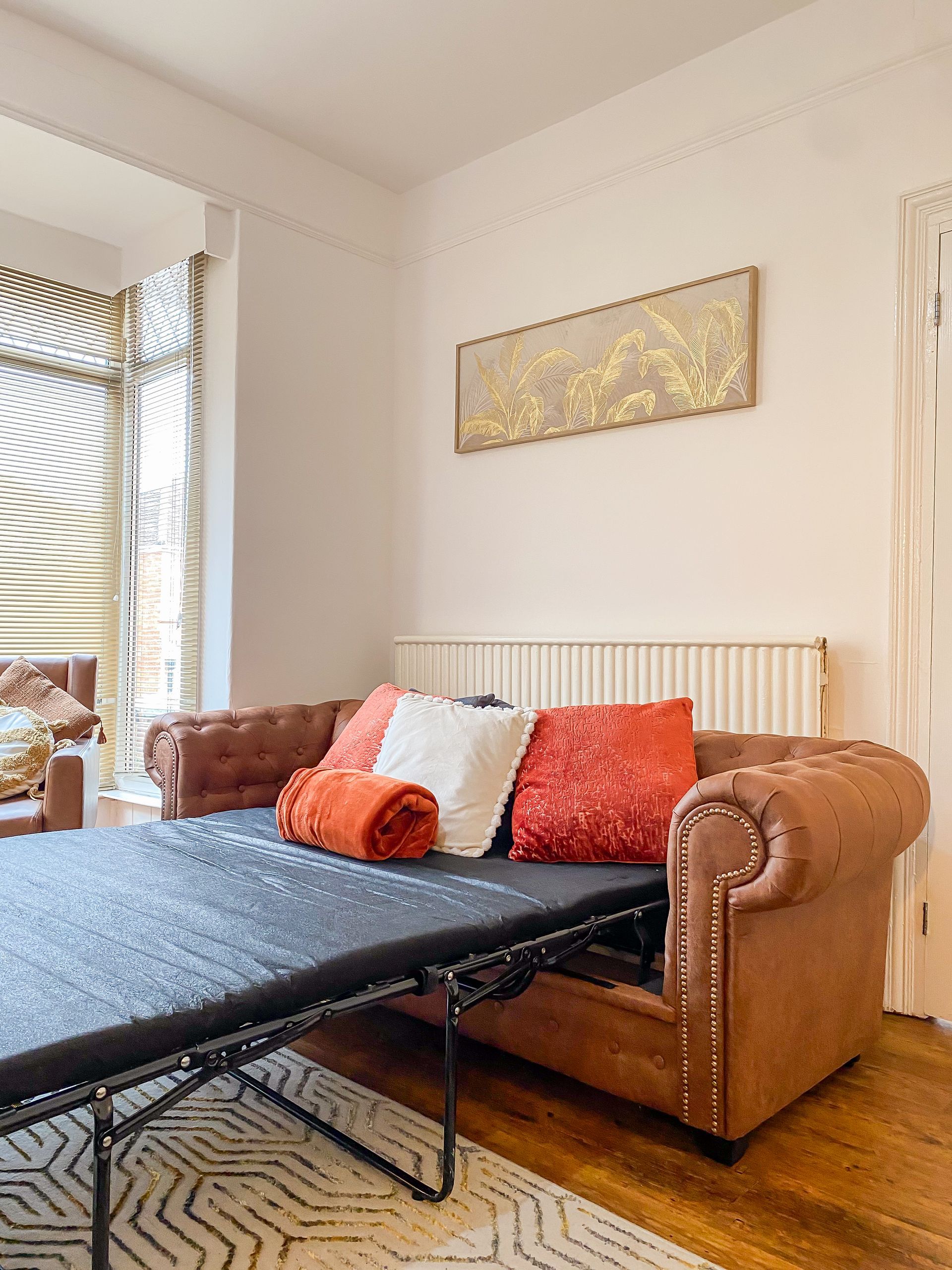 Living room with brown leather sofa, blue sofa bed, and orange cushions by a window