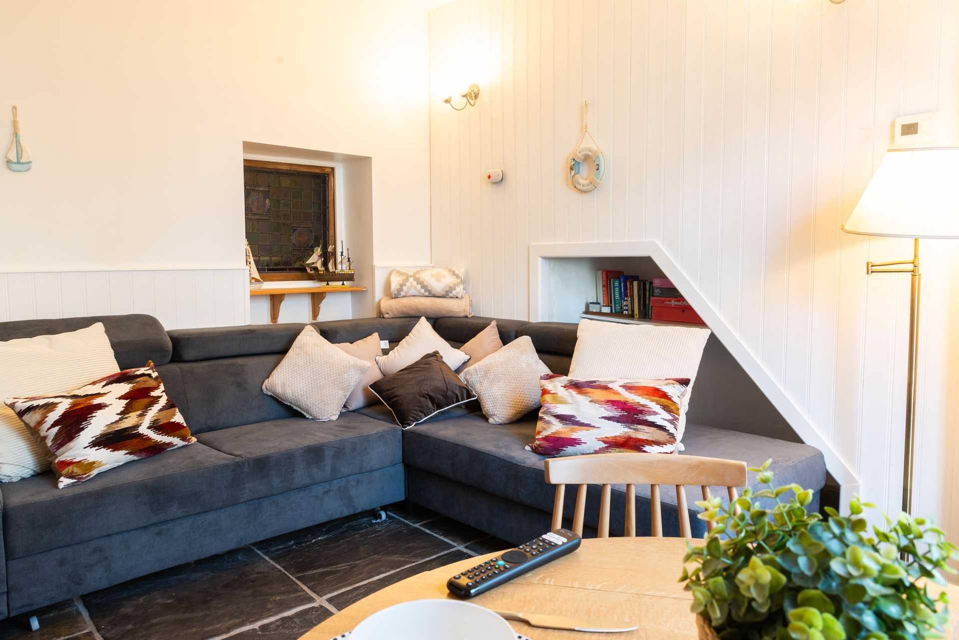 Modern living room with dark gray sectional sofa, patterned cushions, coffee table, lamp, and potted plant.