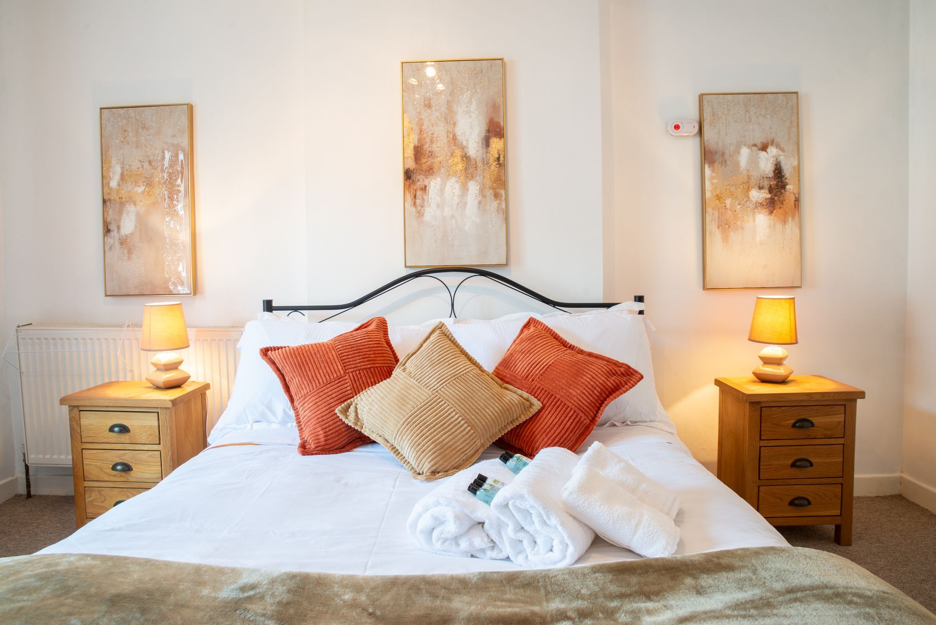 Bright bedroom with a white bed, orange pillows, bedside lamps, and abstract wall art