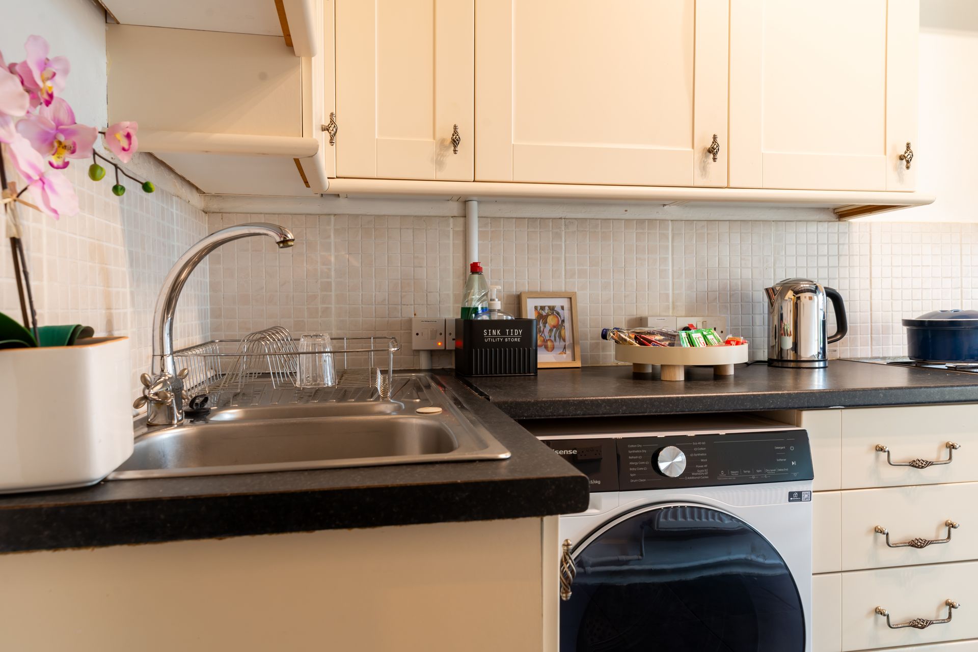 Small kitchen with sink, countertop, orchid, and washing machine under cabinets