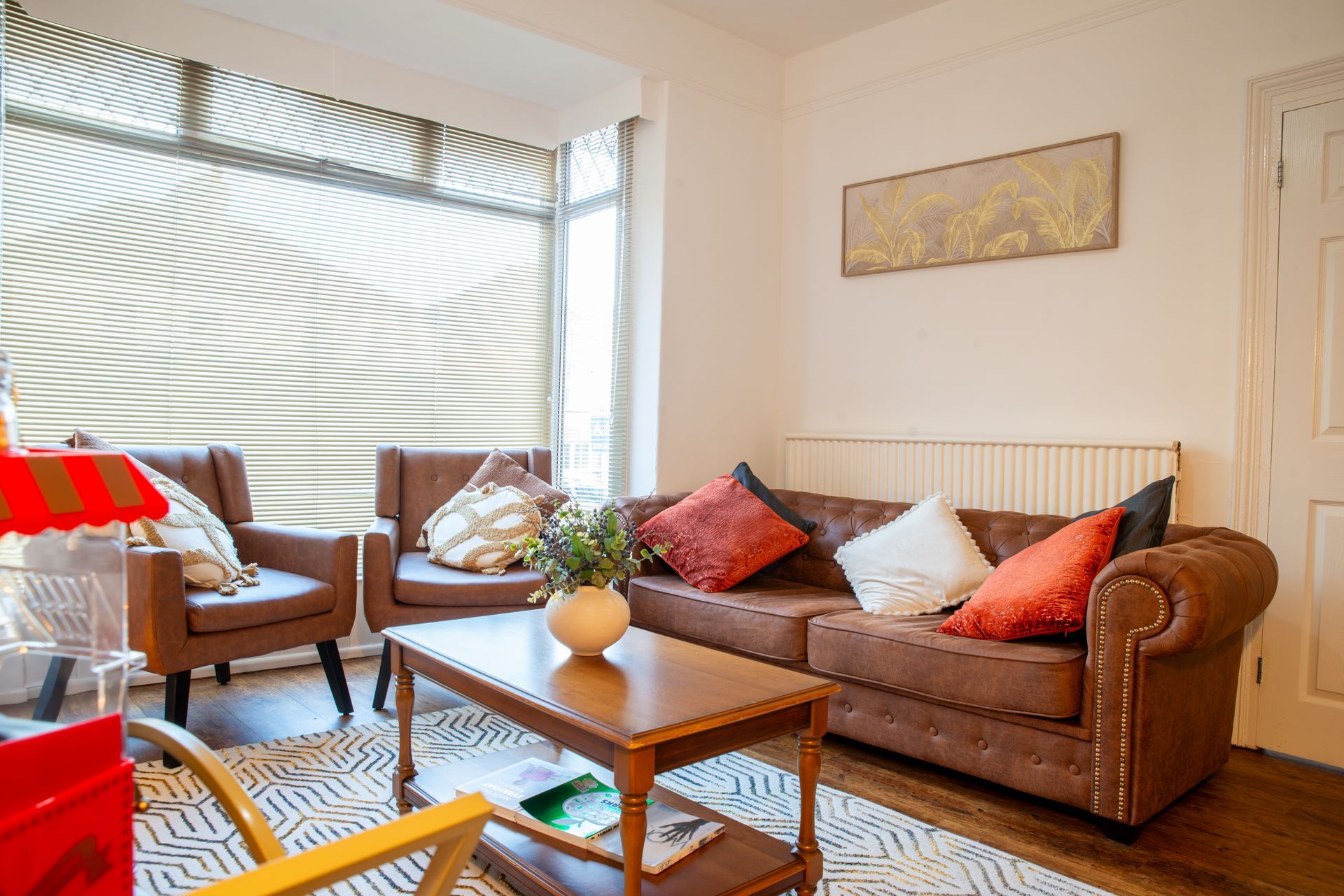 Cozy living room with brown sofa, wicker chair, coffee table, and large window with blinds