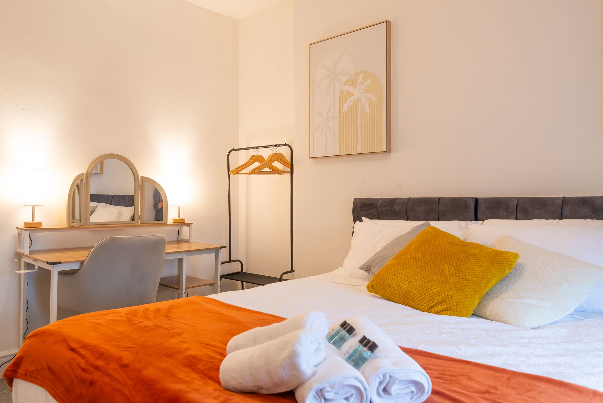 Cozy bedroom with orange bedspread, vanity desk, floor lamp, and framed wall art