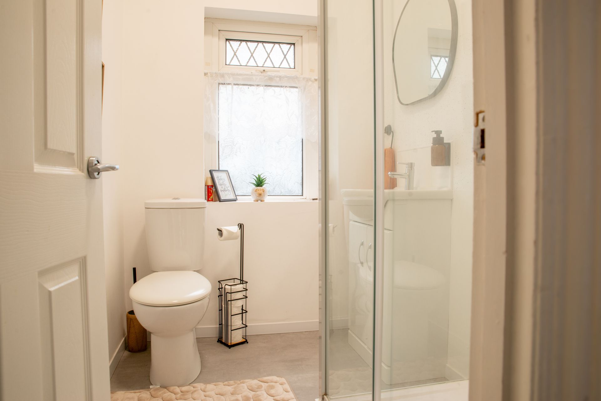 Bright bathroom with toilet, sink, window, and glass shower enclosure