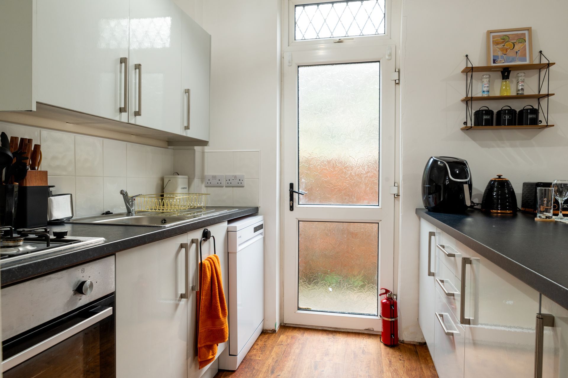 Bright, narrow kitchen with white cabinets, black counters, and a glass back door at the end.