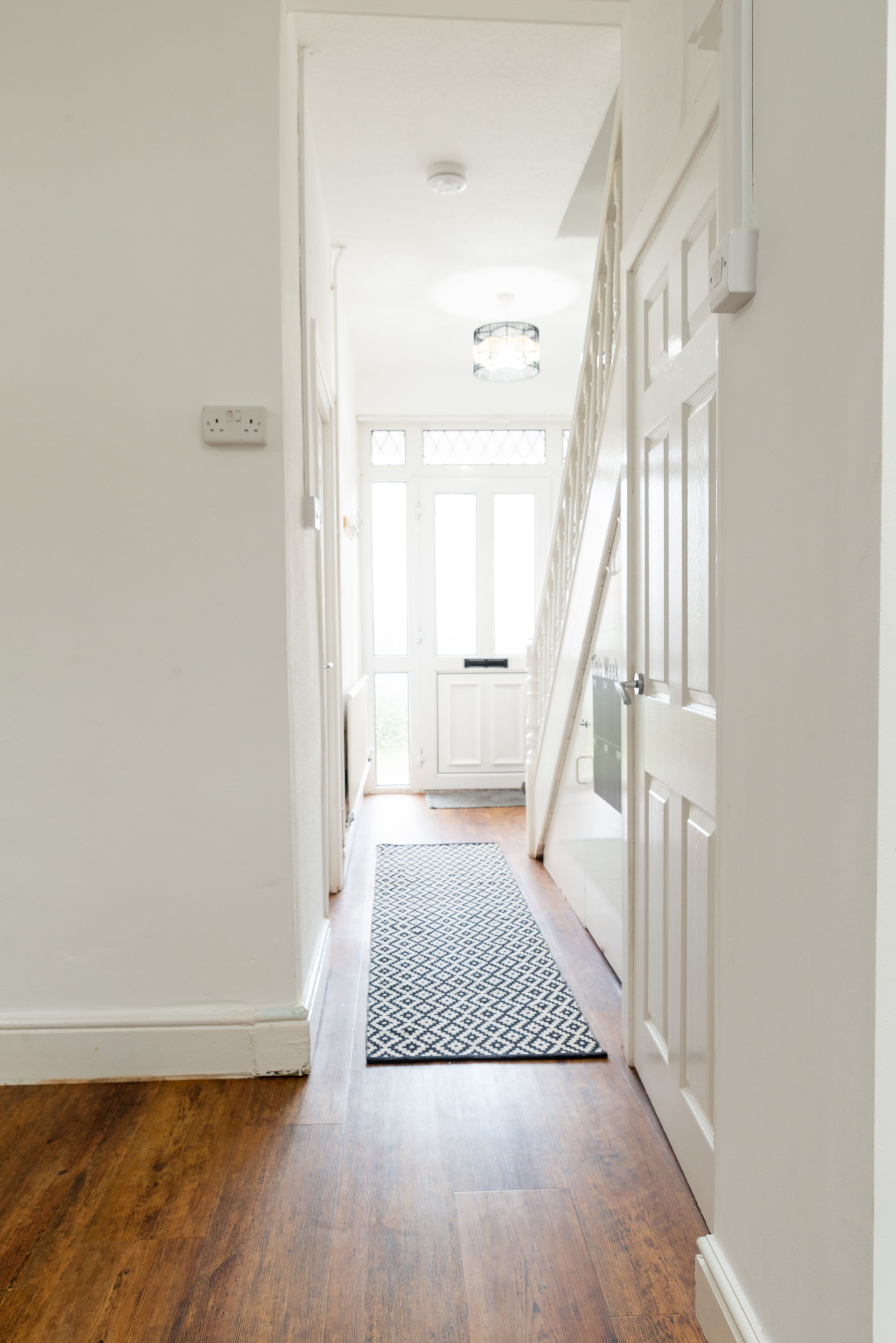 Narrow white hallway with wood floor, front door, rug runner, and a ladder leaning against the wall.