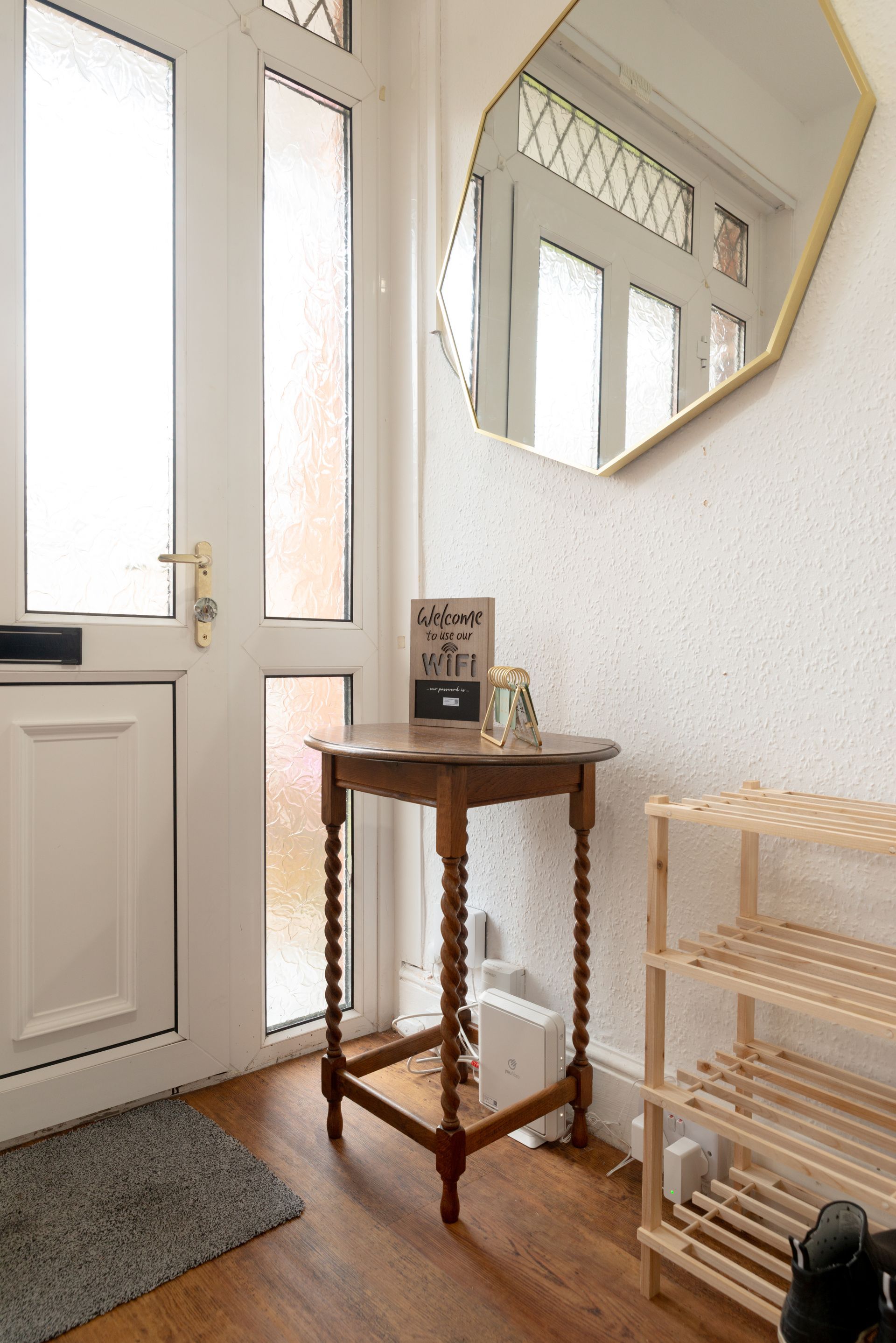 Small entryway with a white door, wooden table, mirror, wicker shelf, and gray mat.