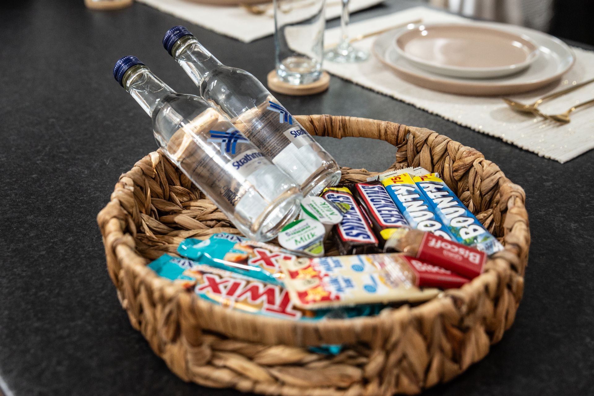 Wicker basket with bottled water, candy bars, and snacks on a dining table