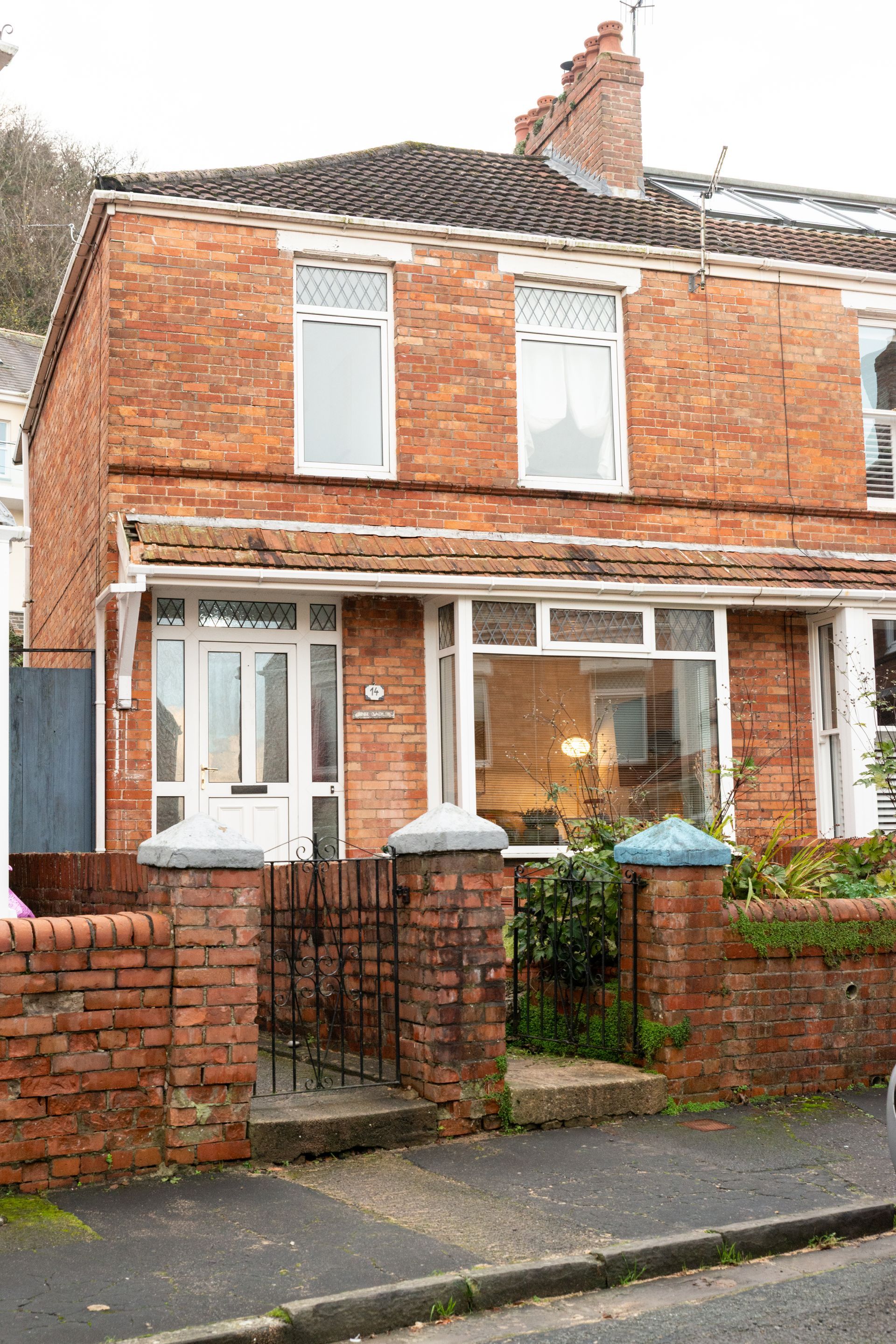 Red brick terraced house with white-framed windows, small front gate, and a street-facing garden wall