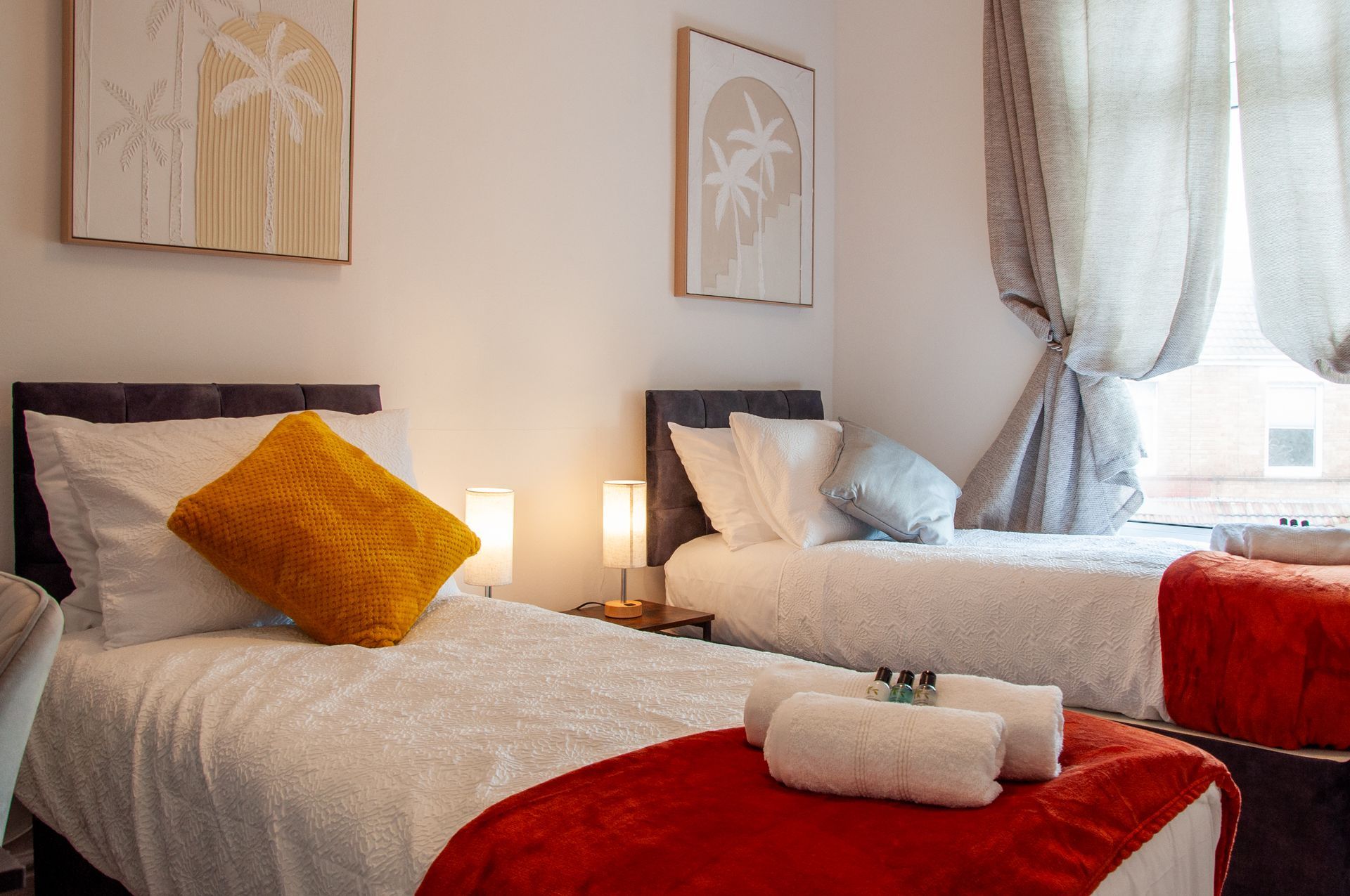Cozy bedroom with two twin beds, red throws, yellow pillow, and soft natural light by the window