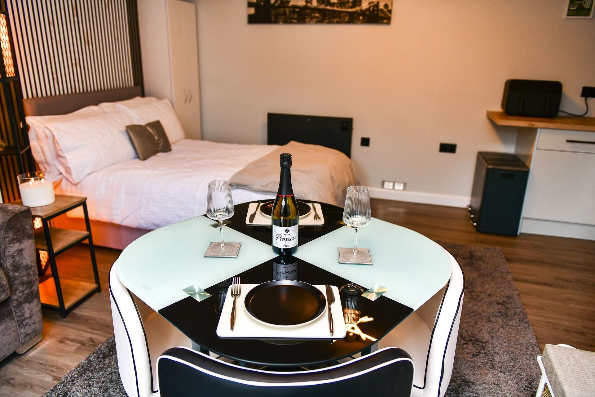Small hotel room with bed, round dining table set for two, and kitchenette area
