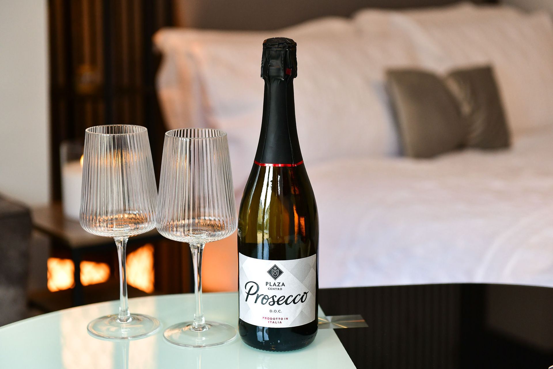 Bottle of prosecco with two empty wine glasses on a table in a softly lit bedroom