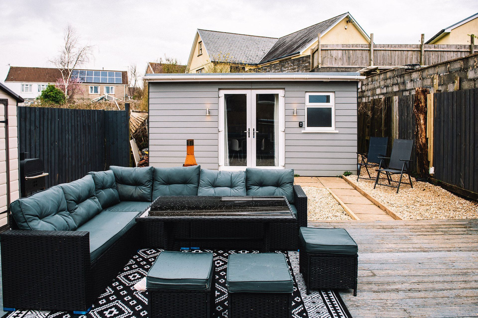 Backyard patio with dark teal sectional sofa, table, and small gray shed under overcast sky