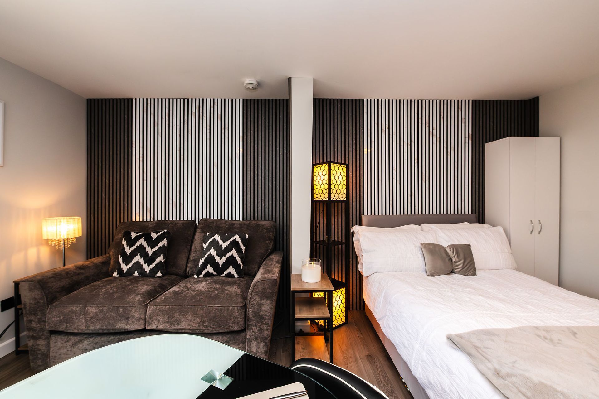 Cozy room with gray sofa, white bed, striped wall decor, and warm lamp lighting