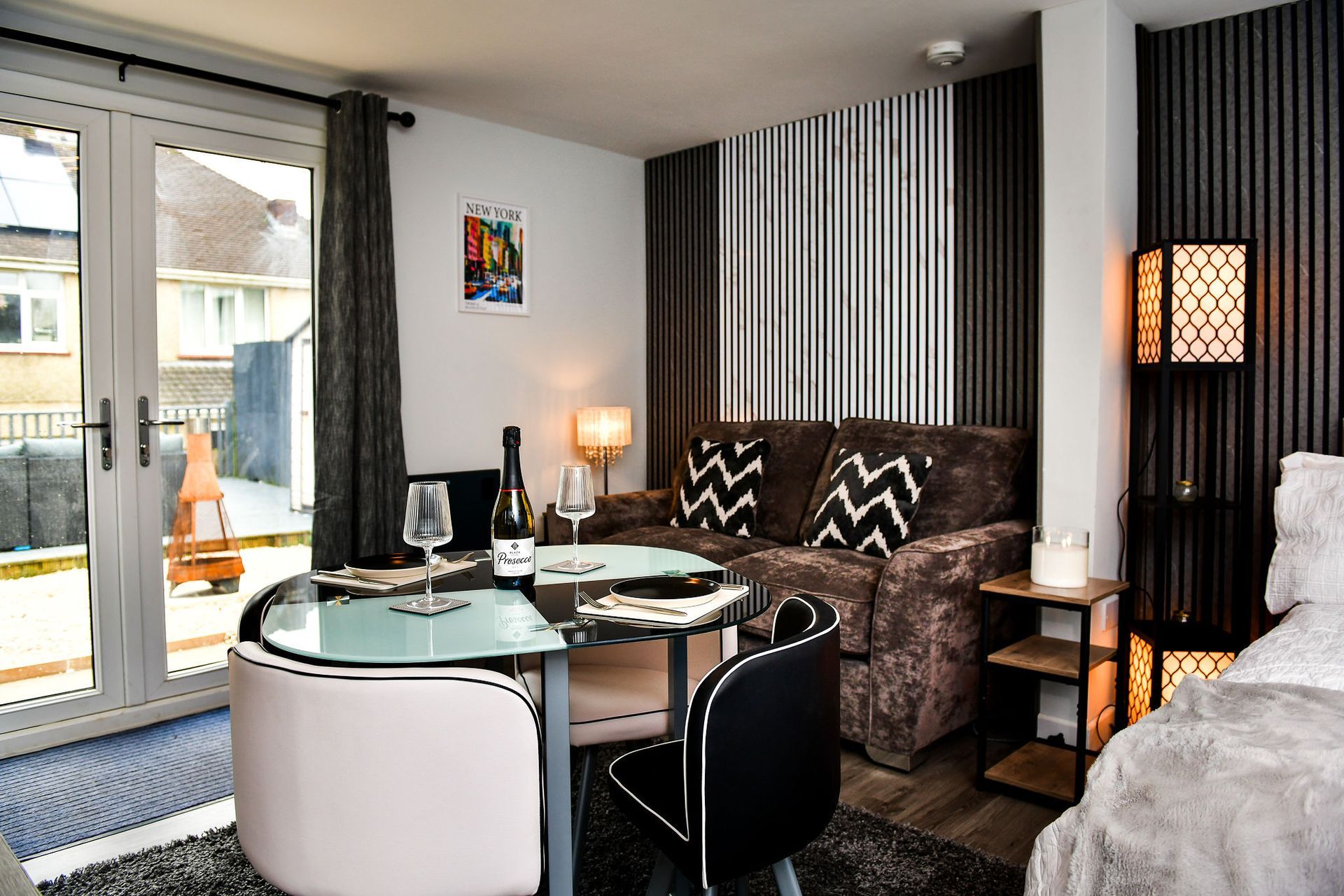 Modern living room with glass dining table, patterned sofa, lamp, and sliding glass doors to a balcony