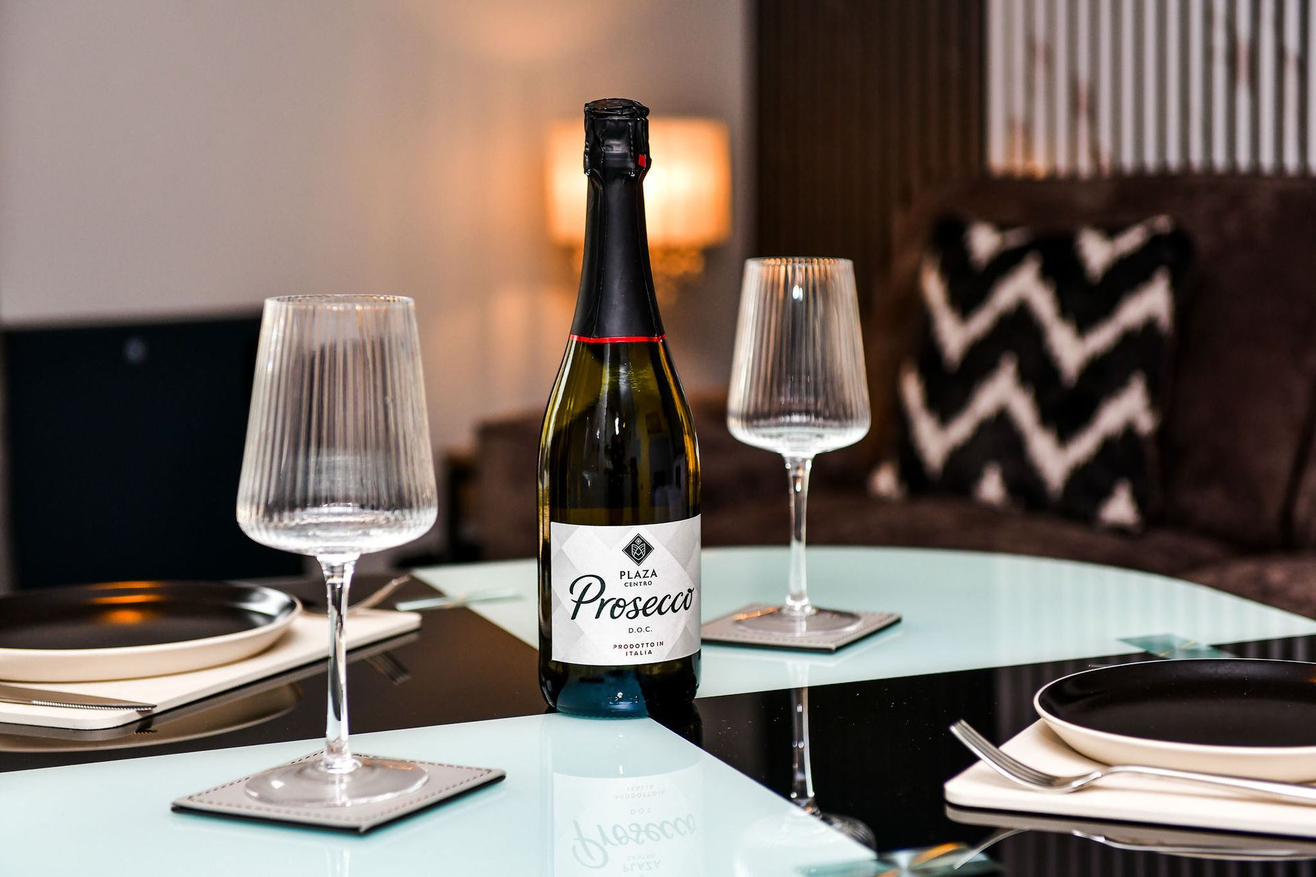 Wine bottle and two empty glasses set on a dining table with plates and a candlelit background