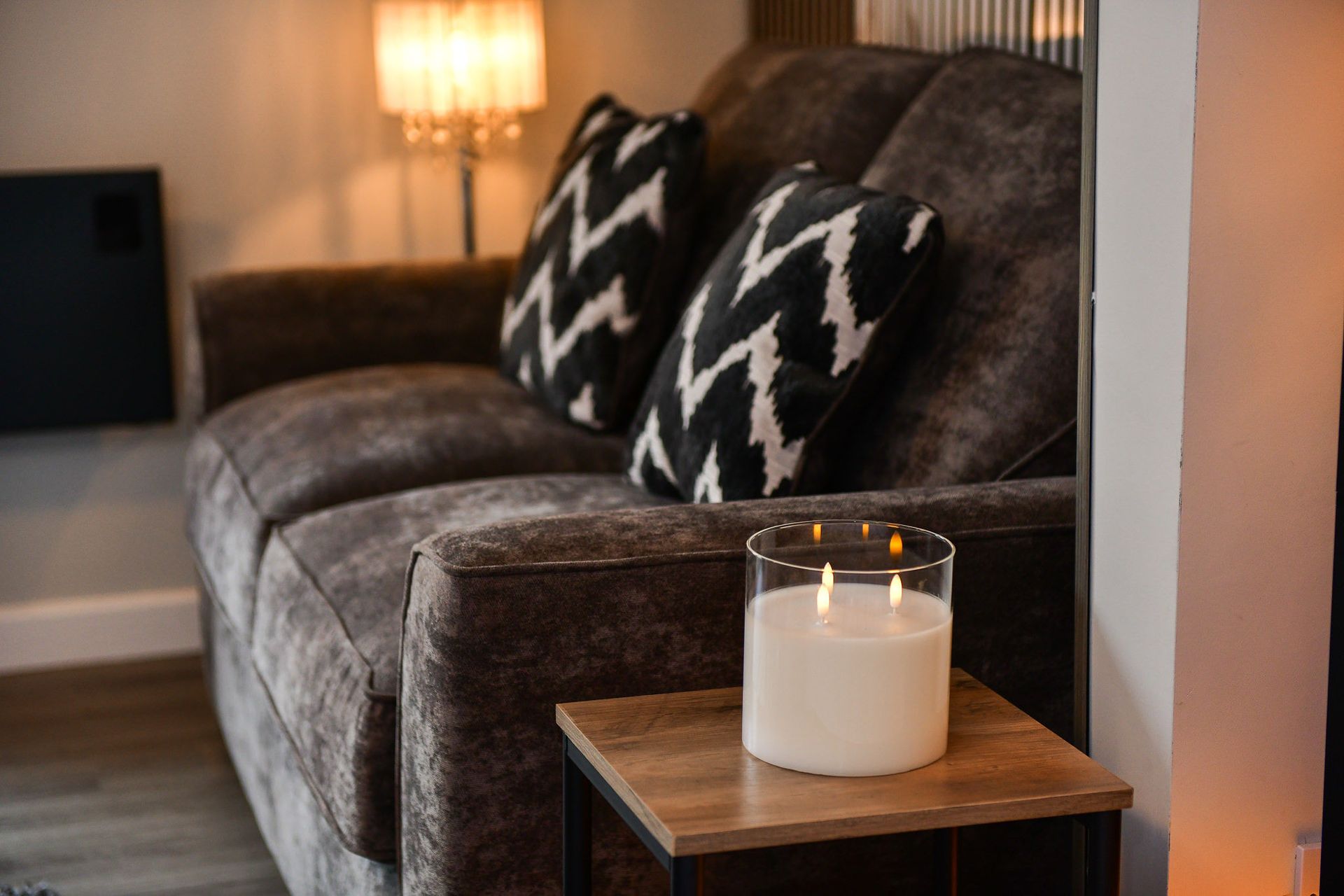 Gray sofa with black-and-white pillows beside a side table holding a lit candle in a cozy living room