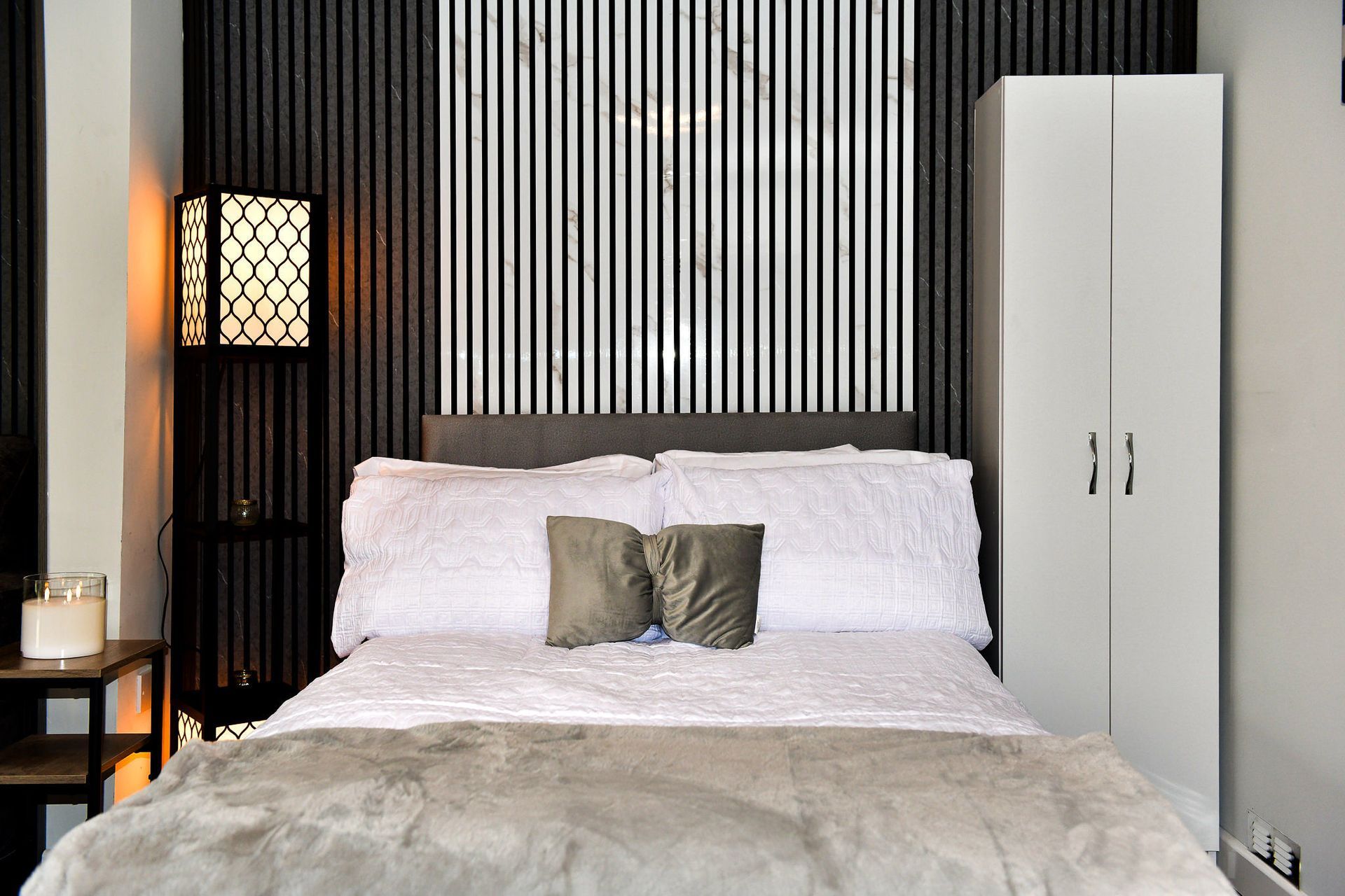 Modern bedroom with a white bed, black striped wall, and white wardrobe