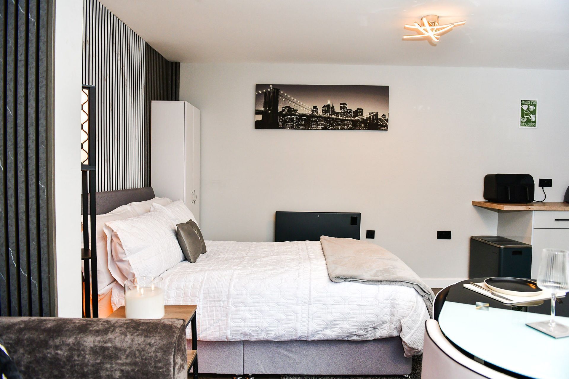 Modern studio bedroom with bed, desk, kitchenette, and city skyline wall art