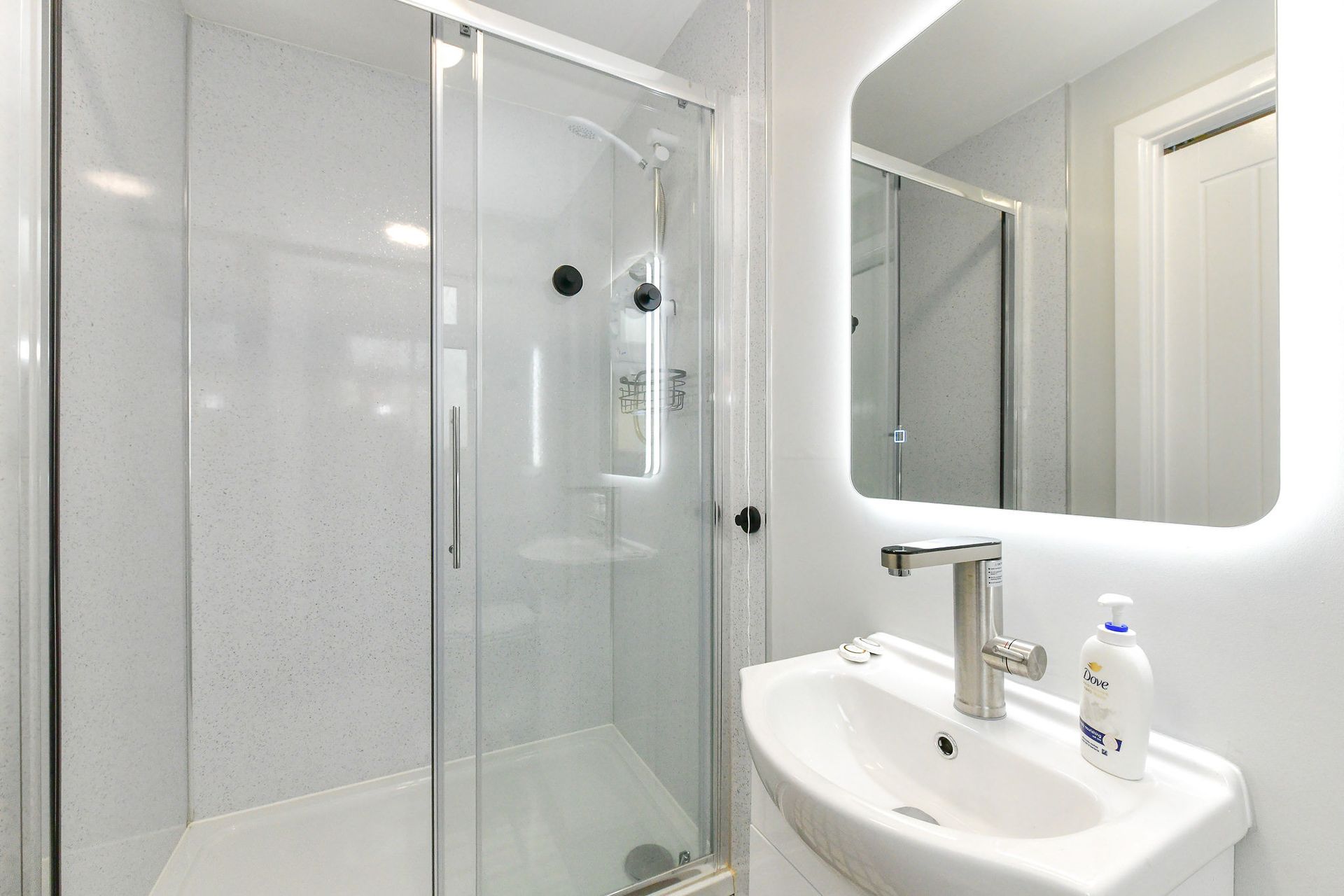 Bright modern bathroom with glass shower, white sink, and illuminated mirror.