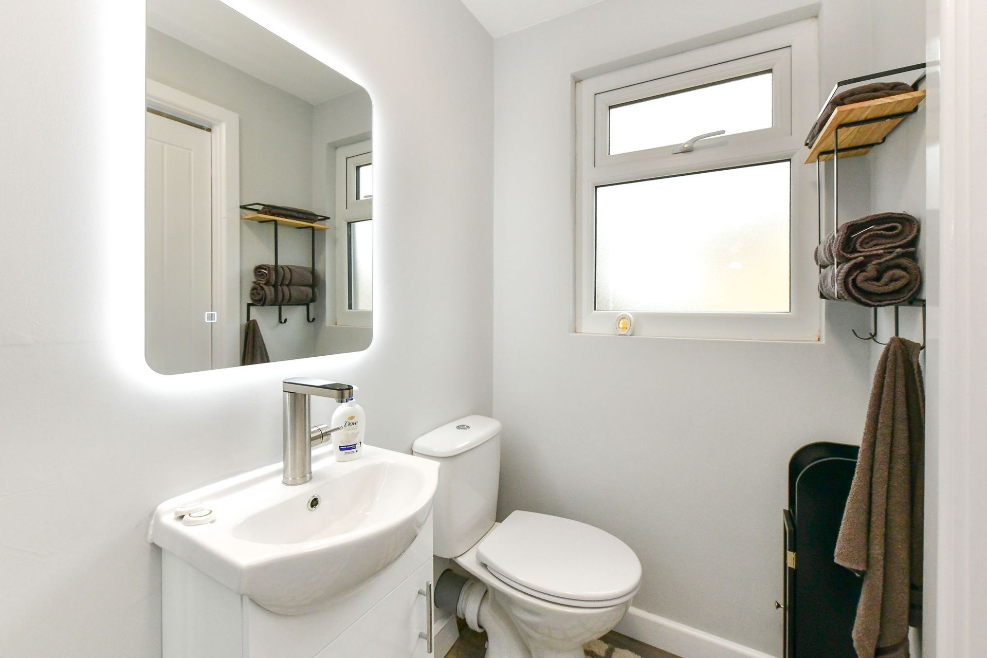 Small white bathroom with sink, mirror, toilet, window, and towel rack.