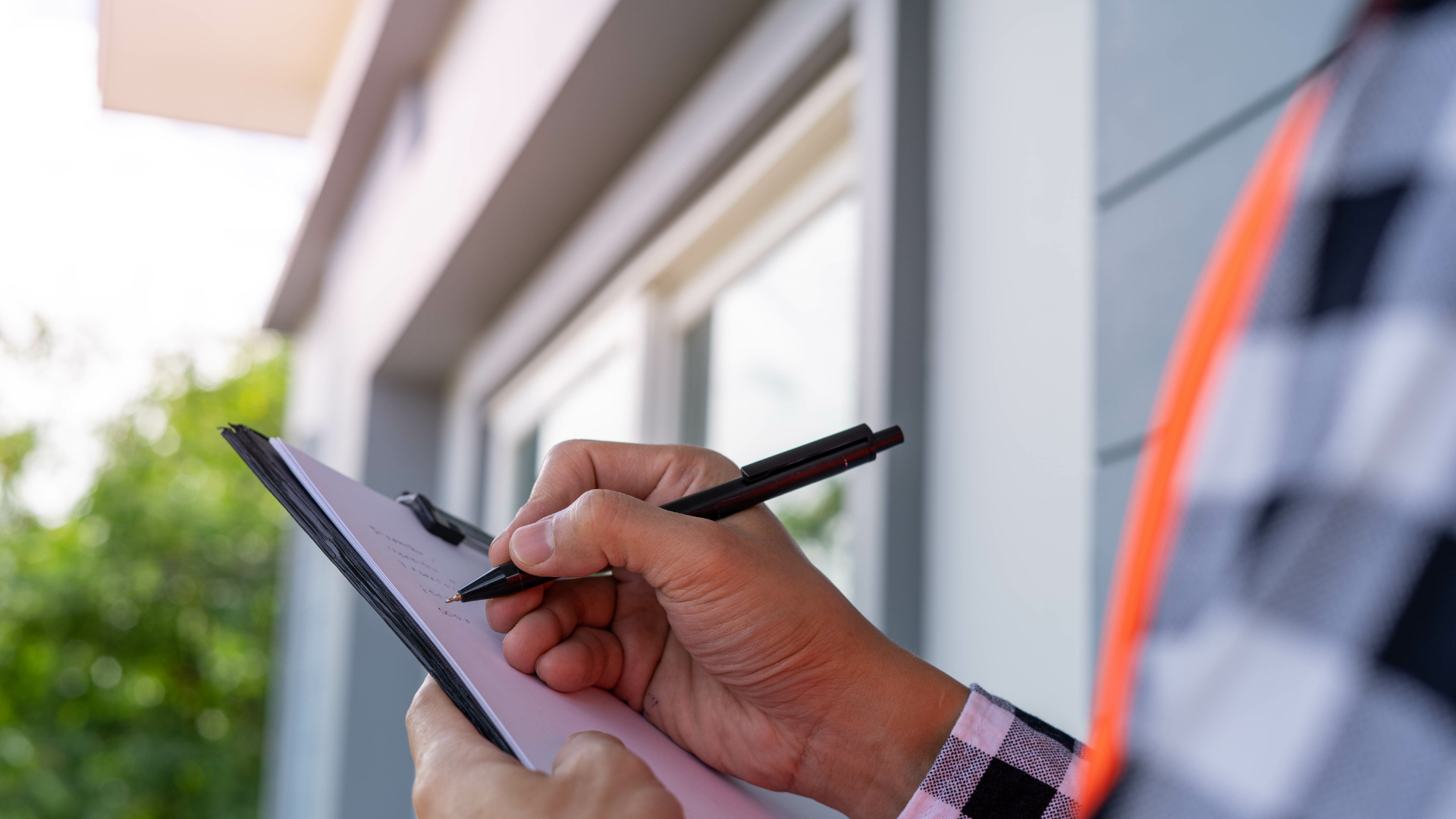 Hand holding a pen and writing on a clipboard outdoors beside a building