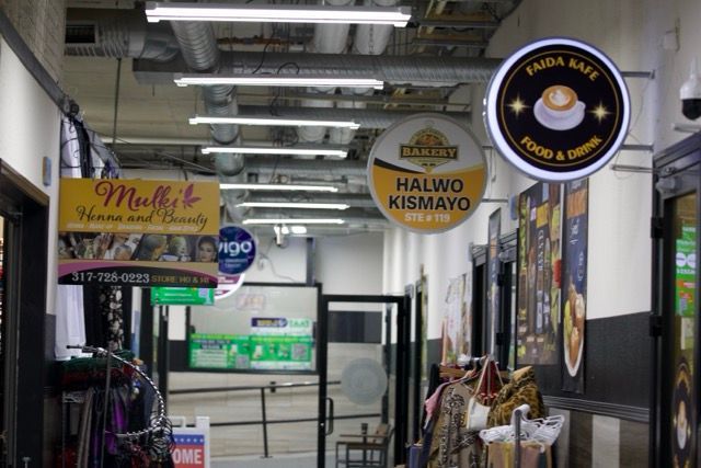 A narrow shopping corridor with colorful signs, including a cafe, beauty salon, and gelato shop.