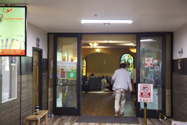 Person entering a prayer room through glass doors. Inside, people are seated. A sign on the door says