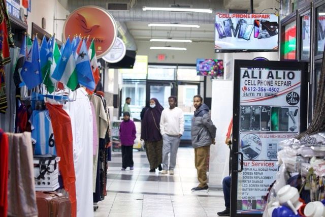 Hallway in a market with shops on the sides, flags hanging, and people walking.