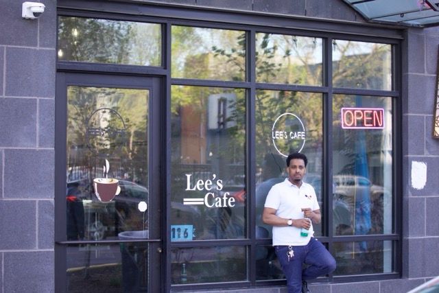 Man standing outside Lee's Cafe, wearing a white polo and blue pants. Open sign in window.