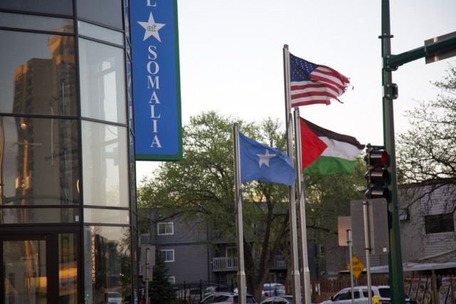 Flags of Somalia, US, and Palestine fly in front of a building with