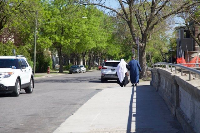 Two people in traditional dress walking down a sidewalk next to a road with cars.