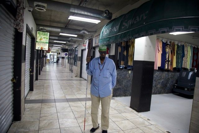 Man with a cane stands in a mostly empty shopping arcade with closed storefronts.