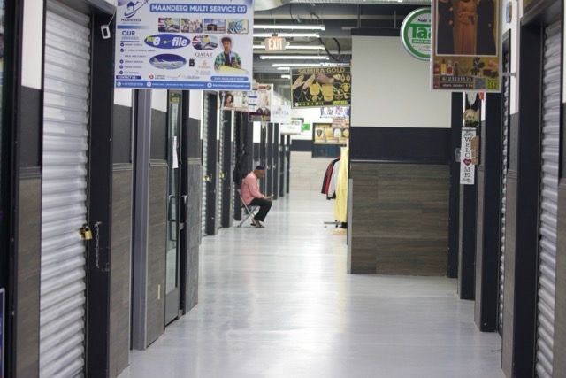 Hallway with closed shop doors; a person sits on the floor in the distance.
