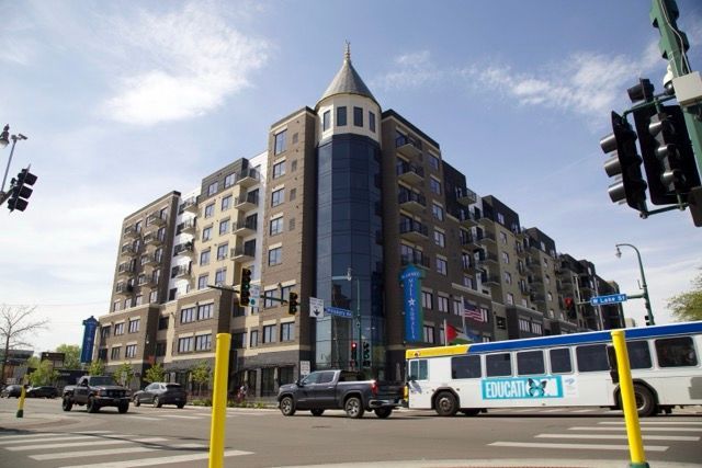 Multi-story brick building with a blue glass tower, street intersection, and a city bus.